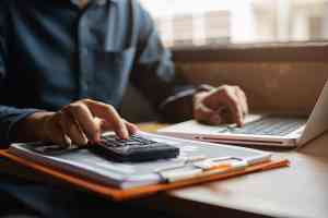 Person mit Taschenrechner und Laptop